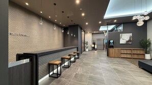 A modern reception area with a brick wall, a reception desk, and a row of wooden benches. - Hotel Route Inn Grand Maebashi (Maebashi)