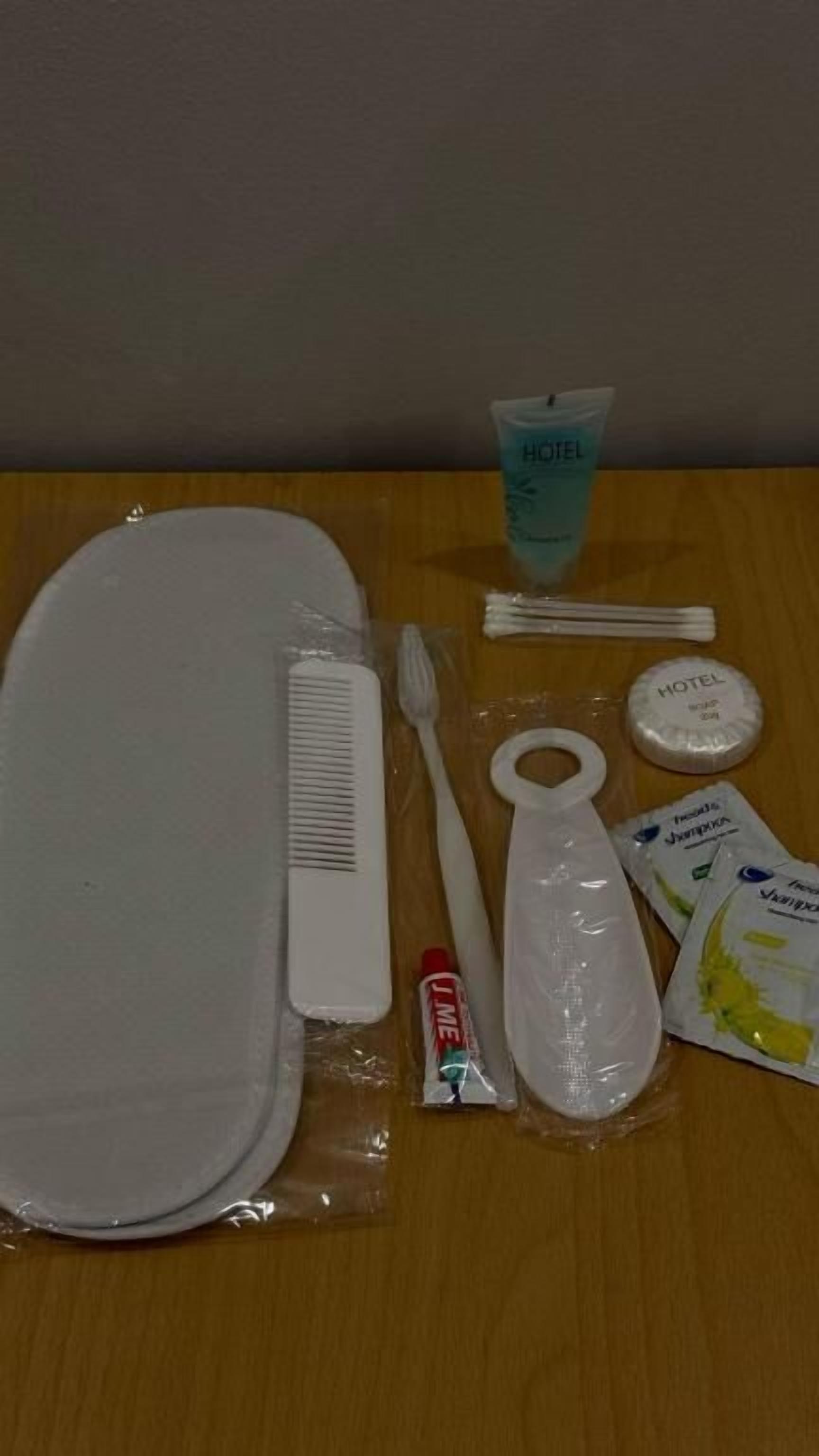 A hotel room with a bed, a toothbrush, a comb, a tube of toothpaste, a cup, and a small container.