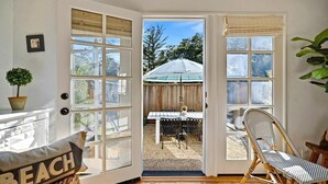 Una habitación con un amplio ventanal que da a un patio exterior con una mesa, sillas, una planta en maceta y una silla de mimbre.