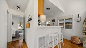 Una cocina moderna con armarios blancos, una isla central con taburetes, una lámpara colgante y una pared de detalles de piedra.