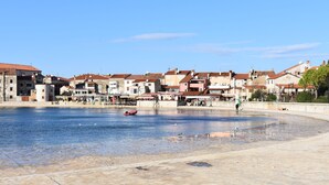 Eine Uferpromenade mit Steinbauten, blauem Himmel und einem roten Boot im Wasser.