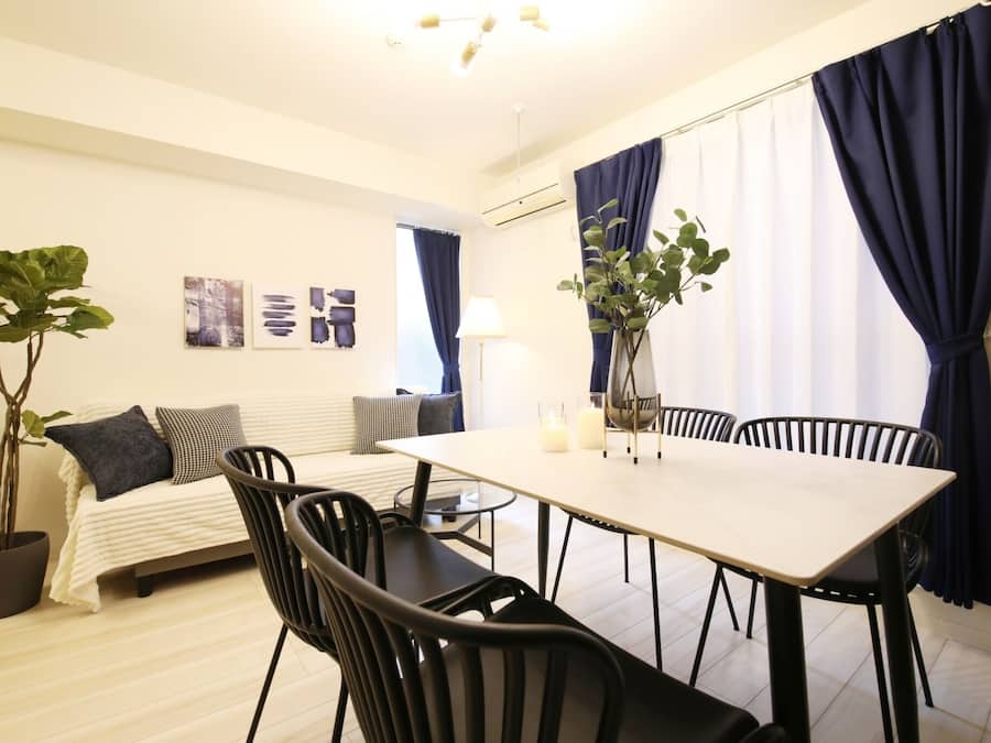 A modern room with a bed, a dining table with chairs, a potted plant, and artwork on the wall.