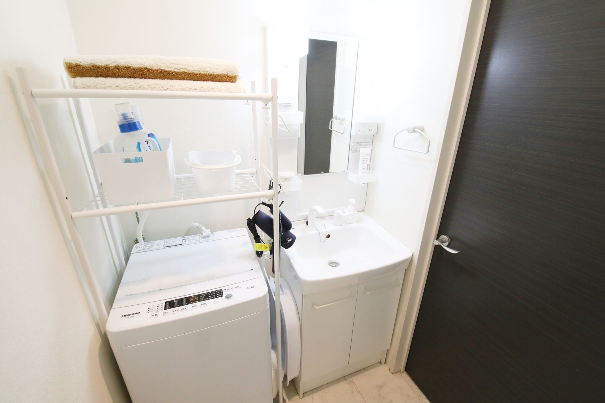 A compact bathroom with a washing machine, a sink, and a towel rack.