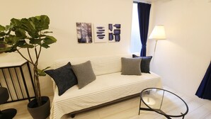 Una sala de estar moderna con un sofá, una mesa de vidrio, una planta en maceta y arte abstracto en la pared.