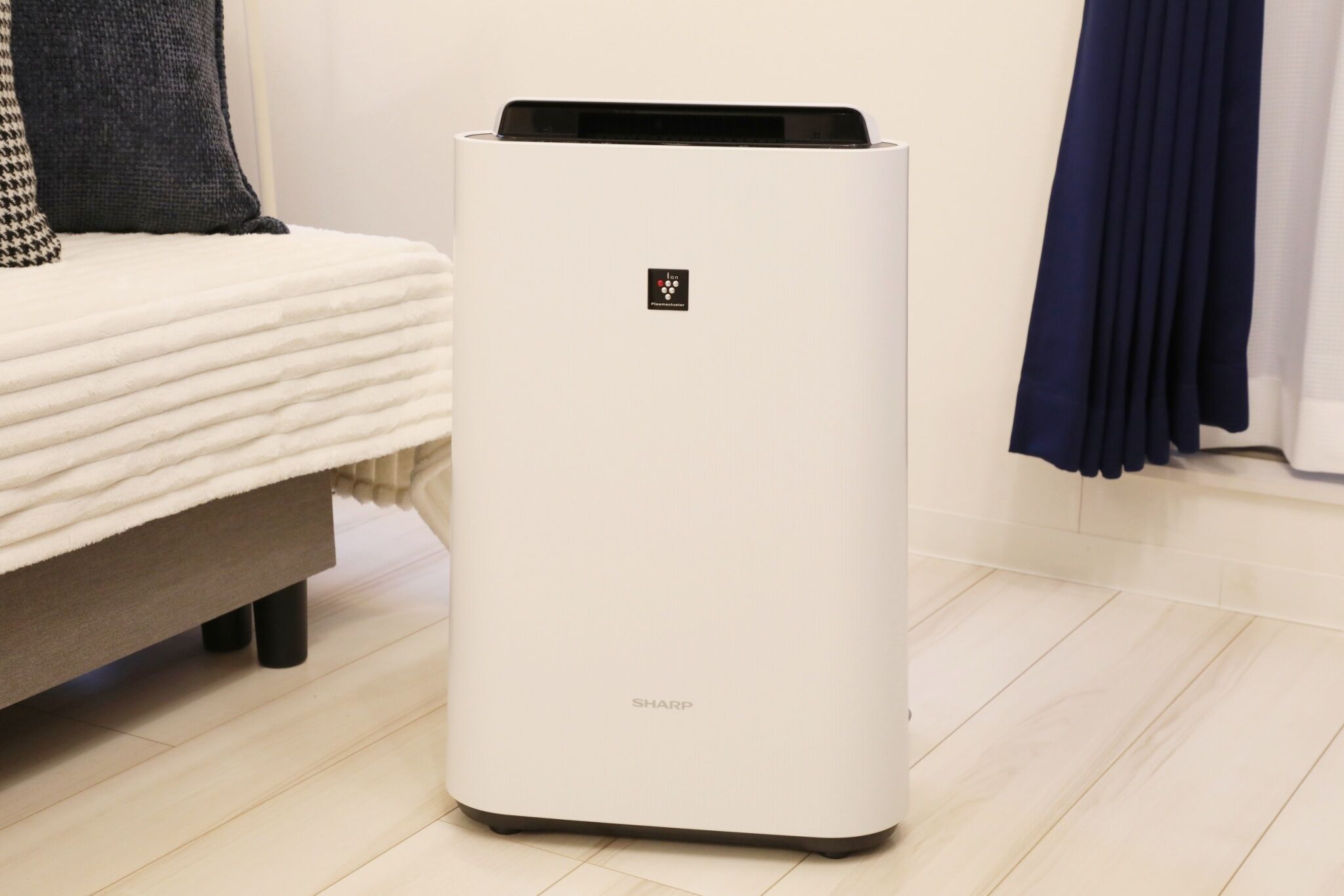 A white air purifier with the brand name 'SHARP' on a light wooden floor.