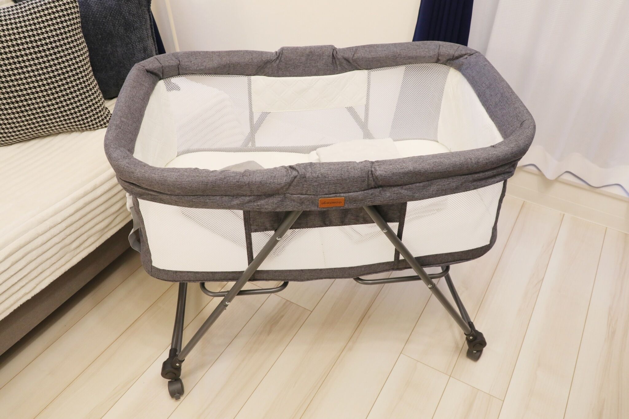 A portable baby crib with a mesh base and a padded top, featuring a foldable stand with wheels for easy mobility.