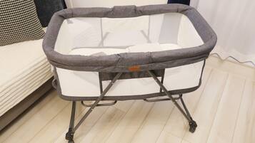 A portable baby crib with a mesh base and a padded top, featuring a foldable stand with wheels for easy mobility.