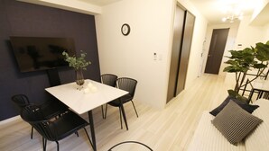 Una sala de estar moderna con un televisor de pantalla plana montado en la pared, una mesa de comedor con sillas y un sofá con cojines.