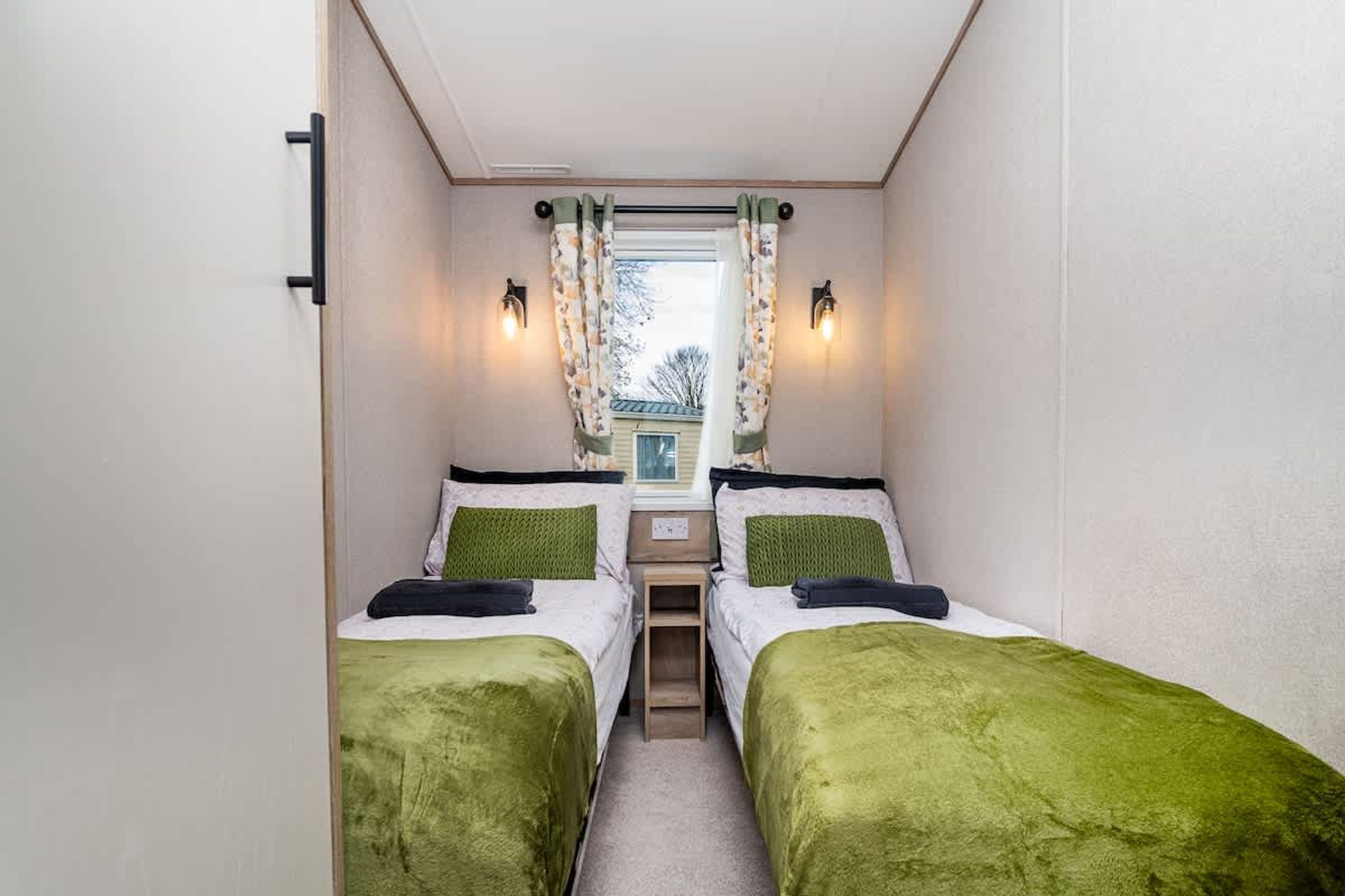 Ein gemütlicher Raum mit zwei Betten, einem kleinen Tisch und einem Fenster mit Vorhängen.