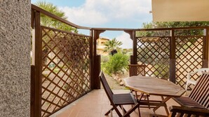 A patio with a wooden table and chairs, a view of a garden, and a lattice fence. - With private garden and air conditioning (Castelsardo)