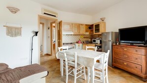 A compact kitchen with white cabinetry, a dining table with chairs, a TV, and a refrigerator. - With private garden and air conditioning (Castelsardo)
