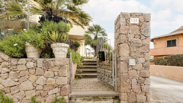 A stone staircase leading to a building with a number plaque, surrounded by potted plants and a stone wall. - With private garden and air conditioning (Castelsardo)