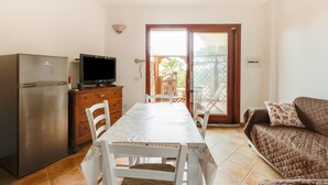 A compact living space with a kitchenette, a dining table, a sofa, and a sliding glass door leading to a balcony. - With private garden and air conditioning (Castelsardo)