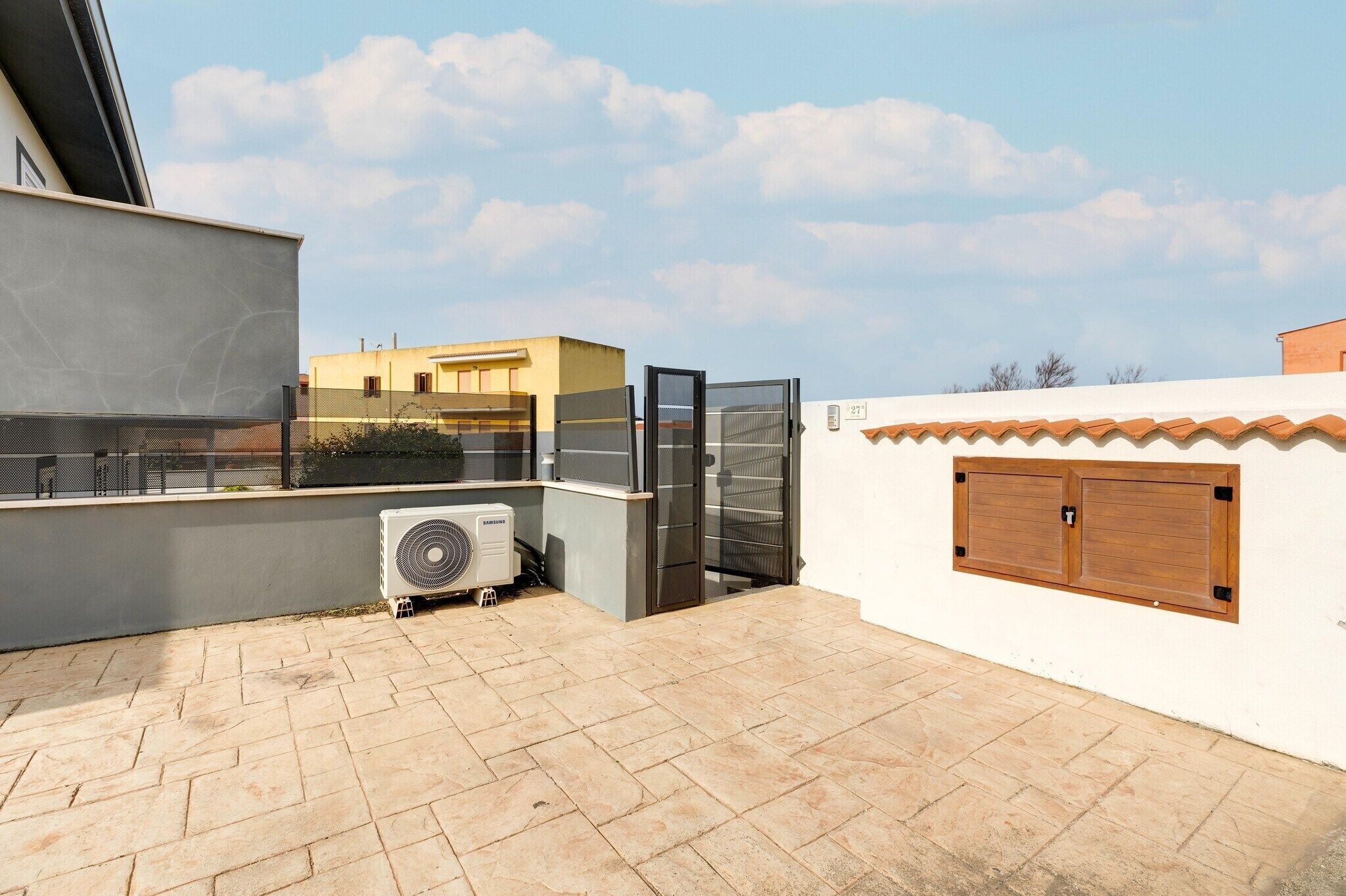 A rooftop terrace with a Samsung air conditioner, a glass door, and a white wall with a wooden door.