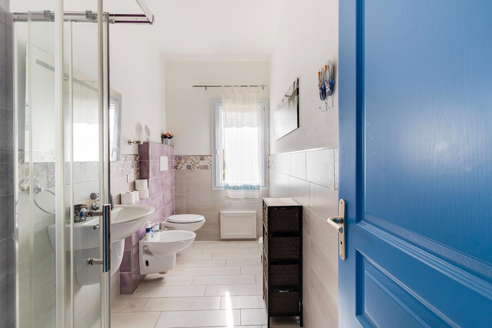Une salle de bain avec une douche à parois de verre, un lavabo blanc, des toilettes et une porte bleue.