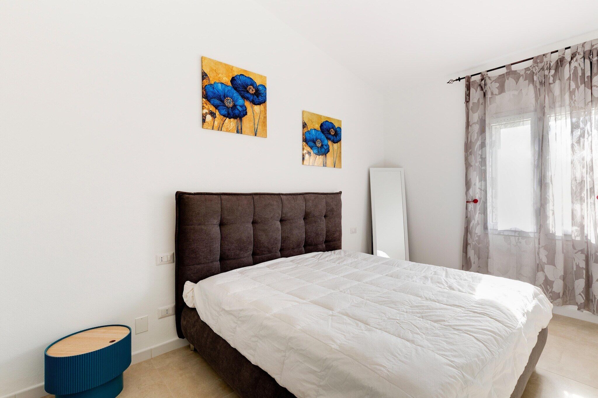 Ein Schlafzimmer mit einem Bett, einem Nachttisch, einem Spiegel und zwei an der Wand hängenden Bildern.