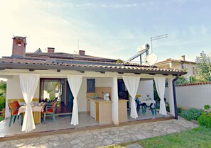 A covered outdoor dining area with a table and chairs, a small kitchen area, and a satellite dish on the roof. - Garden Apartment in Umag (Umag)