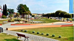 A park with a paved walkway, benches, and trimmed hedges. - Garden Apartment in Umag (Umag)