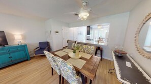 Un coin repas avec une table en bois, des chaises à motifs, une commode turquoise et un ventilateur de plafond.