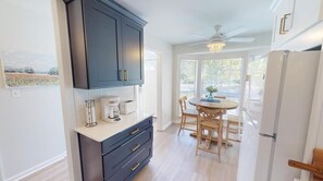 Une cuisine moderne avec des meubles de couleur sombre, un plan de travail blanc et un coin repas comprenant une table et des chaises en bois.