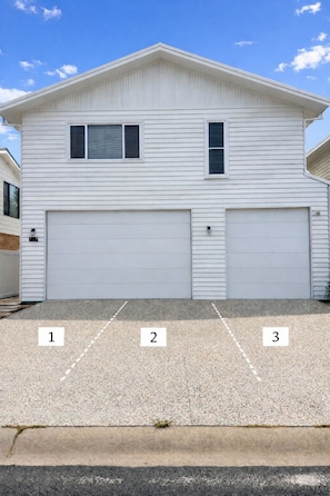 A two-story white house with two garage doors and a driveway with three numbered parking spaces. - 'Bentwood Escape' 
Modern unit in heart of Yamba (Yamba)