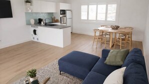 A modern kitchen with white cabinets, a built-in oven, and a dining area with a wooden table and chairs. - 'Bentwood Escape' 
Modern unit in heart of Yamba (Yamba)