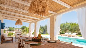 Un tavolo da pranzo in legno con sedie, un lampadario e vista su una piscina e vegetazione.