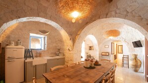 Un interno rustico in pietra con un tavolo da pranzo in legno, pareti in pietra e un angolo cucina con un frigorifero vintage.