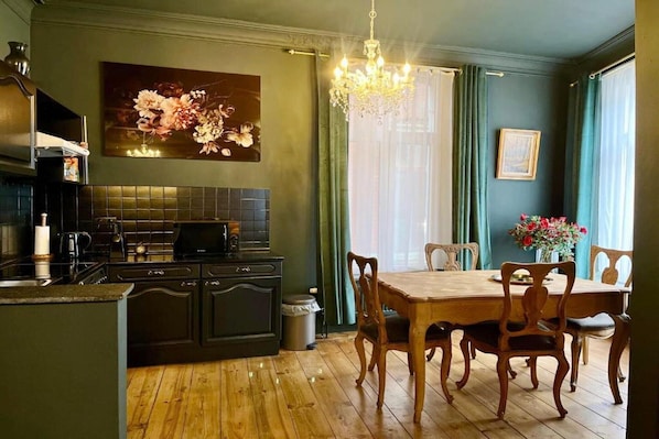 A kitchen with dark cabinetry, a wooden dining table, and chairs. There is a chandelier hanging above the table.