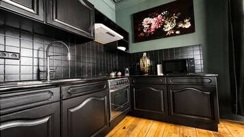 A kitchen with black cabinetry, a tiled backsplash, a wooden floor, and a microwave.