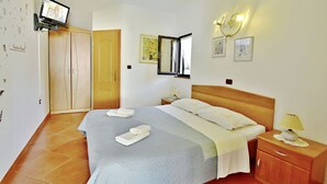 A hotel room with a large bed, a wooden wardrobe, a television mounted on the wall, and a bedside table with a lamp. - Cozy Flat With Garden Access in Umag (Umag)