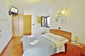 A hotel room with a large bed, a wooden wardrobe, a television mounted on the wall, and a bedside table with a lamp. - Cozy Flat With Garden Access in Umag (Umag)