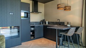 Una cocina moderna con armarios oscuros, un microondas integrado, una campana extractora de acero inoxidable y una encimera de mármol. Hay dos taburetes de bar y un pequeño cubo de basura.