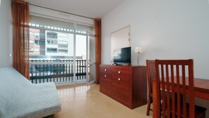 Habitación de hotel con cama, un escritorio de madera, televisión y vistas a un balcón con barandilla.
