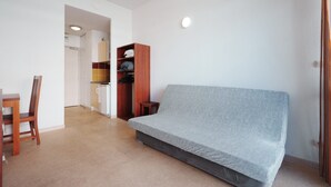 Una habitación con una cama, una silla de madera, una mesita y una zona de kitchenette.