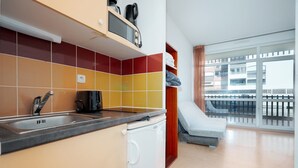 Una cocina con un lavamanos, una cafetera y un lavavajillas. Hay un balcón con vistas a edificios.
