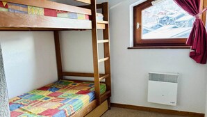 Un lit superposé avec une couverture aux couleurs vives, une fenêtre donnant sur un beau paysage et un climatiseur fixé au mur.