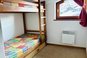Ein Stockbett mit farbenfroher Decke, ein Fenster mit Blick und eine Wand-Klimaanlage.