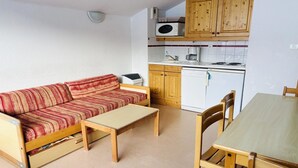 Un espace de vie compact comprenant un canapé, une petite table, des meubles en bois, un four à micro-ondes, une machine à café et un réfrigérateur compact.