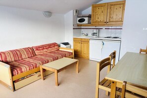 Ein gemütlicher Wohnraum mit einer Couch, einem kleinen Tisch, Holzschränken, einer Mikrowelle, einer Kaffeemaschine und einem kompakten Kühlschrank.