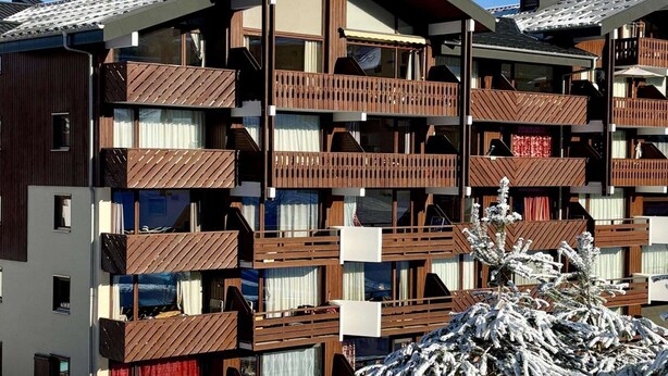 Un immeuble à plusieurs étages, doté de balcons, de grandes fenêtres et d’un arbre recouvert de neige.