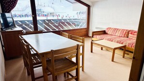Une pièce avec une table et des chaises en bois, un canapé et une grande fenêtre donnant sur un espace extérieur enneigé.