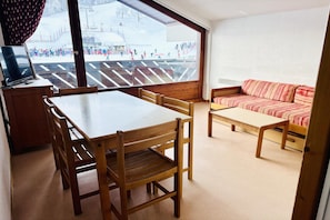 Ein Zimmer mit einem Holztisch und Stühlen, einem Sofa und einem großen Fenster mit Blick auf eine verschneite Landschaft.