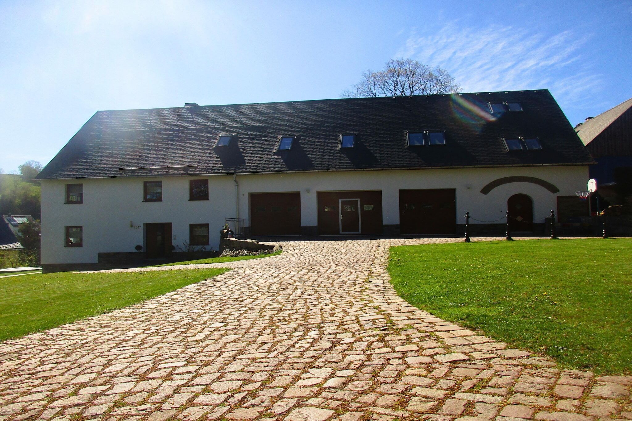 Ein Gebäude mit einem Kopfsteinpflasterweg, der zu einer weißen Fassade mit zahlreichen Fenstern und einem dunklen Dach führt.