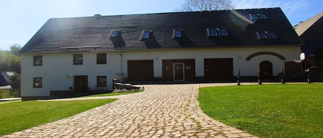 Ein Gebäude mit einem Kopfsteinpflasterweg, der zu einer weißen Fassade mit zahlreichen Fenstern und einem dunklen Dach führt.