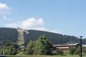 Una montaña con un telesilla, un edificio con paneles solares y una colina boscosa.