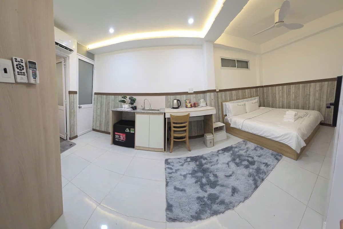A compact hotel room with a bed, a desk, a chair, a small kitchenette, and a bathroom.