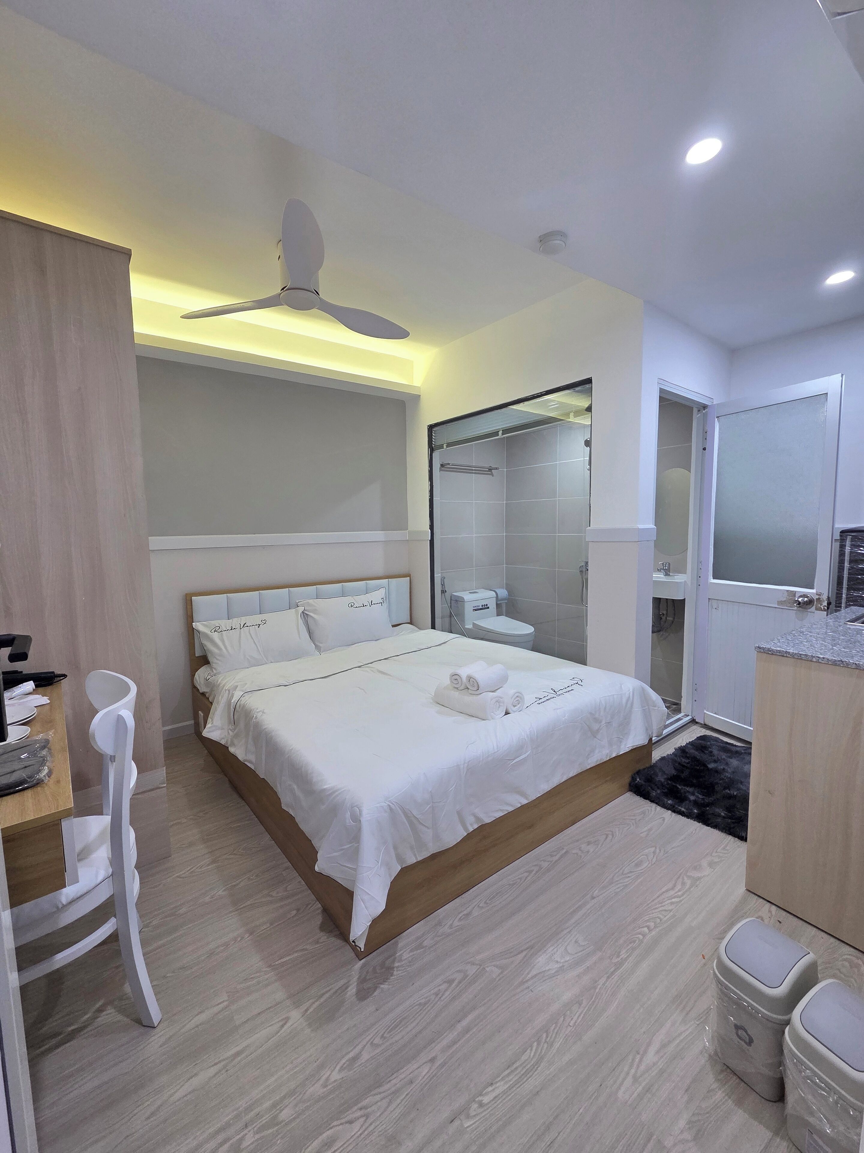 A modern hotel room with a bed, bedside table, chair, and a shower area.