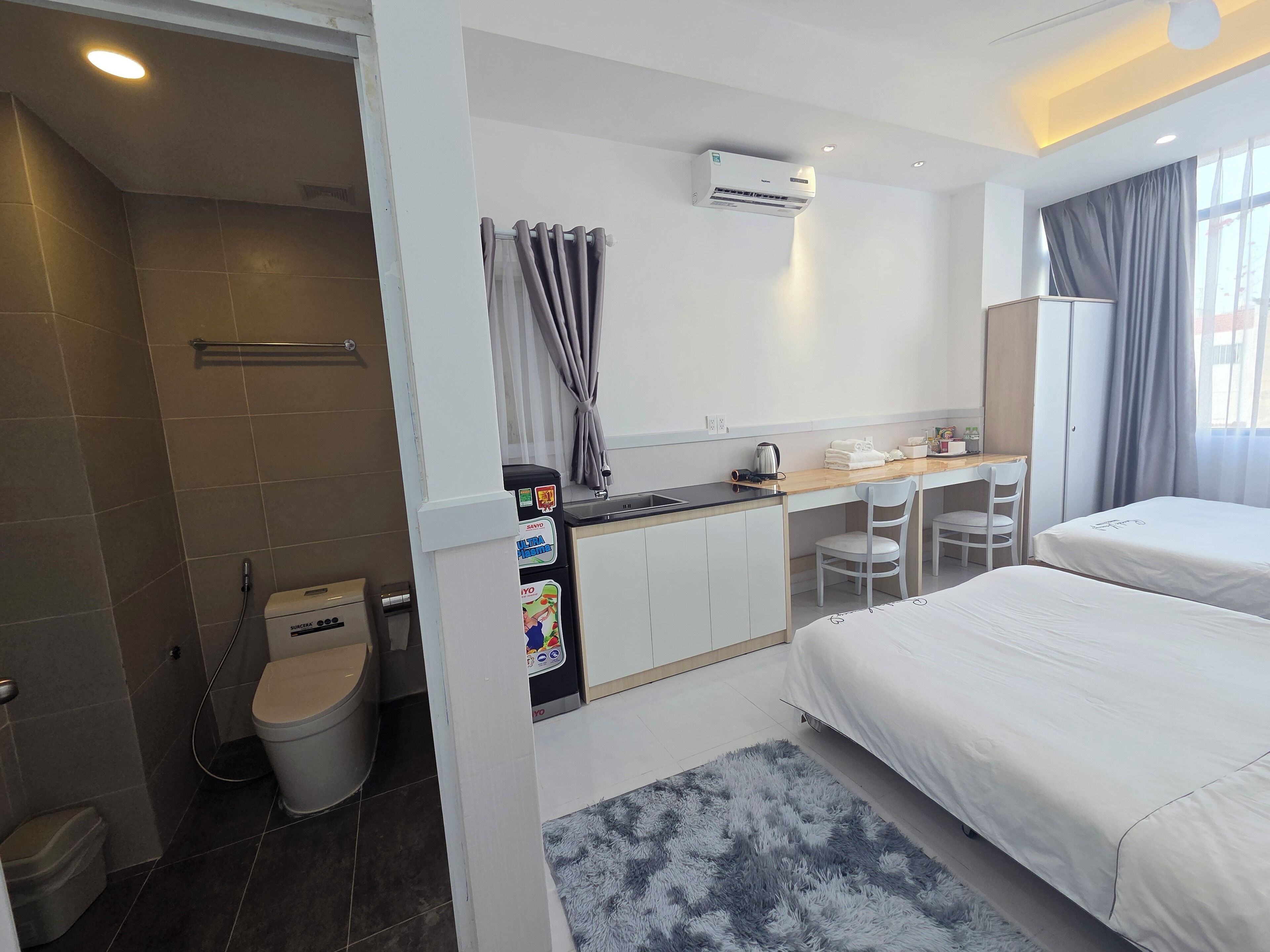 Ein Hotelzimmer mit Dusche, WC, einer Küchenzeile, zwei Betten und einem Vorhangfenster.