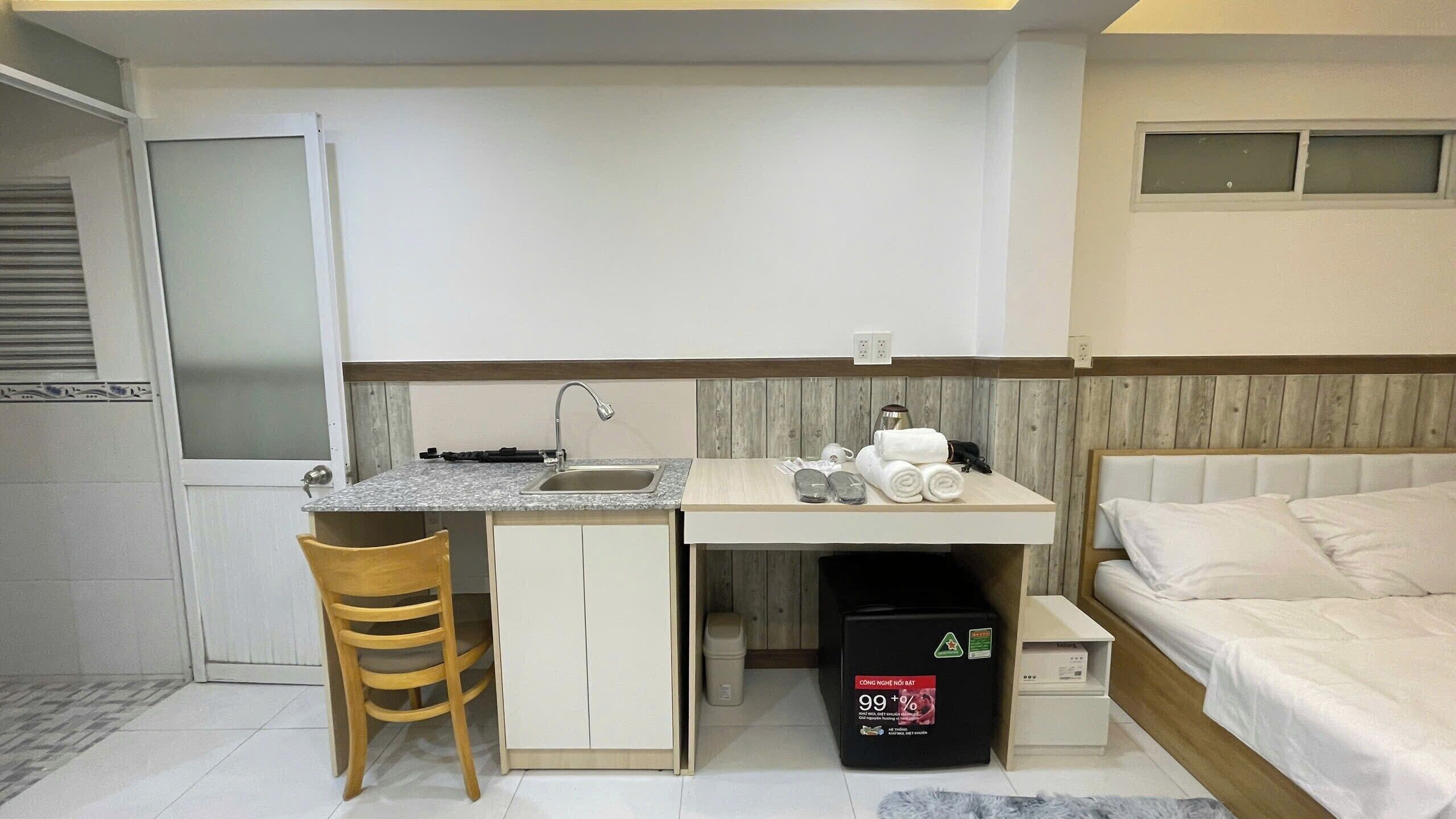 A compact hotel room with a kitchenette, a bed, and a small seating area.